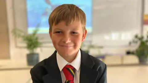 Student Kian in his uniform smiling in a classroom