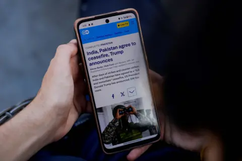 Reuters A man reads news on his mobile phone after the ceasefire announcement between India and Pakistan, in Srinagar May 10, 2025. REUTERS/Sharafat Ali