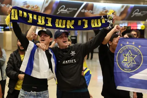 JACK GUEZ/AFP via Getty Maccabi Tel Aviv fans hold up a scarf in the airport before their trip to Amsterdam