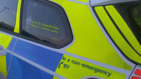 A marked Devon and Cornwall Police car with blue and yellow high viz branding on the side of it. 