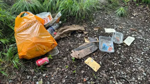 Nicola Millner Rubbish, food plastic containers and carrier bags discarded in the woods by Windermere.