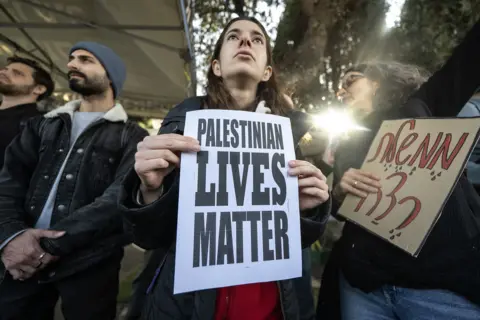 Mostafa Alkharouf / Anadolu via Getty Images A protester stands with a placard reading 'Palestinian lives matter' next to other protesters standing and holding signs as the sun shines through foliage behind them, in West Jerusalem on 31 March.