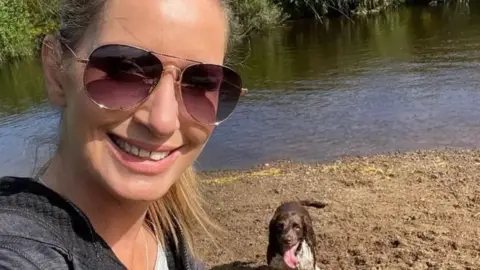 Family photo Nicola Bulley selfie smiling at the camera in sunglasses by the river with a brown and white spaniel by her side panting