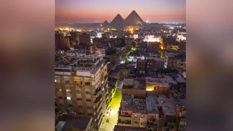 Getty Images The stark contrast between the city of Cairo and the iconic Pyramids make for a stunning view during the blue hour, Cairo, Egypt, Africa
