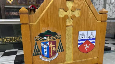 A close up of a brown wooden chair with two brightly coloured coats of arms.