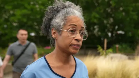 Karen Bonner in her pale blue uniform. She stands outside and wears glasses.