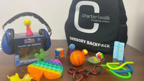Charter Walk Shopping Centre A 'sensory backpack' on a table with many sensory items including ear defenders, and toys of all colours and shapes.