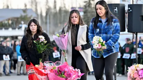 Three women lay flowers at a makeshift memorial on the steps of the town hall in Tumbler Ridge.