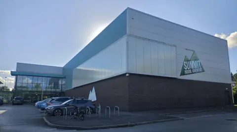 A large warehouse-style building with cars parked outside and bike racks
