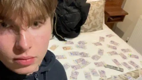 Counter Terrorism Policing A blond young man sitting in a hotel room with ten pound notes and twenty pound notes spread on the bed behind him.