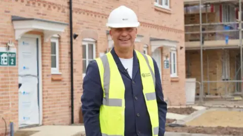 Yorkshire Housing/Michael Foster A man stands on a building site wearing a suit, high-vis vest and a hard hat
