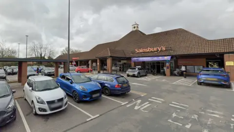 A Sainsbury’s supermarket with a busy car park in front showing several parked cars