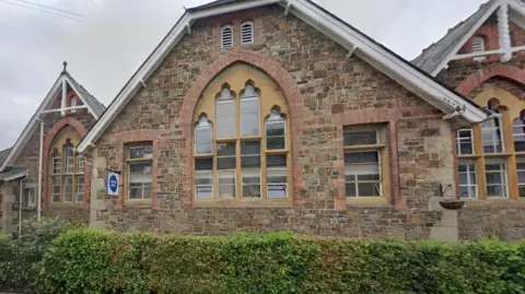 The Ockment Centre in Okehampton, where Citizens Advice is based. It is an old stone building over three blocks with pointed rooves. It has a large arched window with decorative framed glass. A hedge is at the front of the image. 