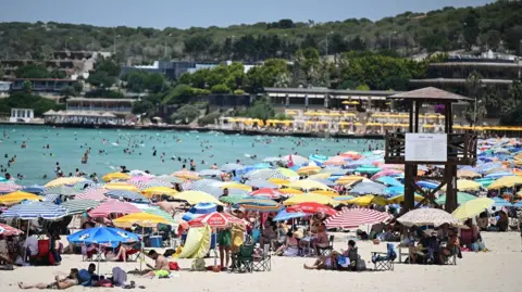 Getty A summer beach scene with hundreds of people under sun shades and a blue sea