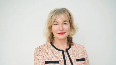 Visit Britain Patricia Yates, a woman with shoulder-length blinde hair, smiles at the camera in front of a white backdrop.