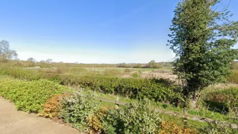 Fields and foliage can be seen as well as wooden fencing.