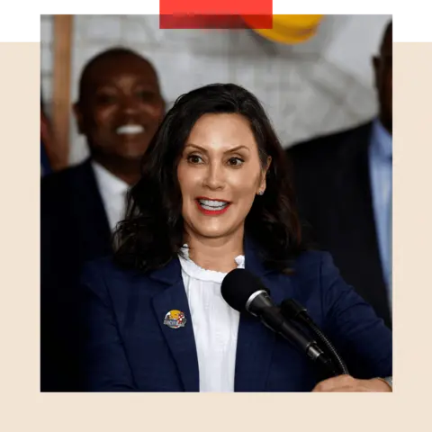 Gretchen Whitmer speaks into a microphone. She is wearing a white short and a navy blue jacket