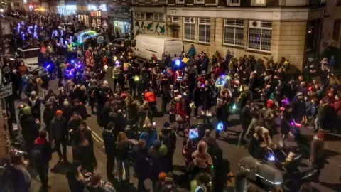 Hundreds of people carry illuminated lanterns along North Street in Bedminster on a dark night during the annual winter lantern parade