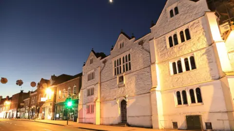 An old white building. It is dusk. The street lighting is on. 