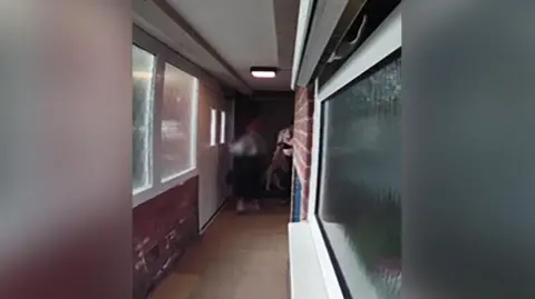Still image taken from doorbell footage of a puppy being held by the scruff of its neck outside a flat.