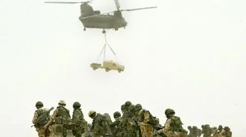 AFP via Getty Images British airmen of the 51st Sqn Royal Air Force regiment observe a Chinook of the RAF joint helicopter force as it lifts a Land Rover vehicle and its trailer during a practice air assault operation design to capture an enemy airfield, at an undisclosed location in the desert outside Kuwait City.