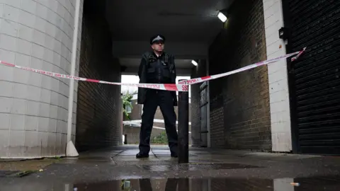 PA Media Police officer and police tape outside the block of flats where a 22-year-old woman was stabbed to death in a fight with a 16-year-old boy