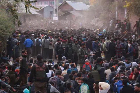NurPhoto via Getty Images Thousands of young men are sitting and standing at a recruitment drive. Some soldiers wearing military fatigues are also visible