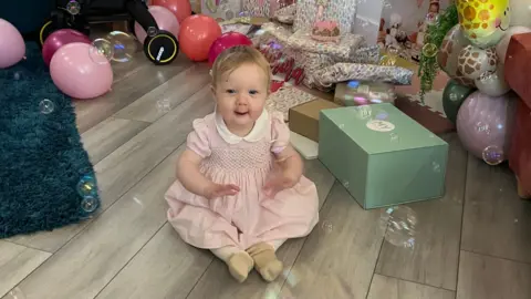 Aurora laughing as bubbles float around her as she sits next to a pile of presents on a living room floor.