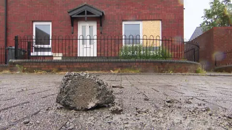 A red terraced house with a rock outside it and boarded up window