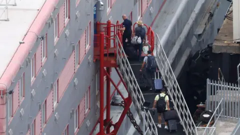 Getty Images Men holding suitcases climbing a set of steps to board a barge