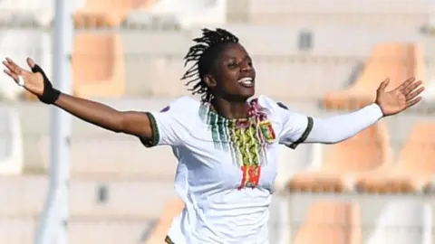 Aissata Traore, wearing a white Mali shirt, spreads her arms out in celebration after scoring against Ghana