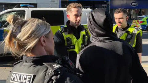 Three police officers speak to a boy wearing a black hoodie