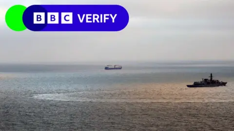 PA Media A photos of two ships. One military vessel can be seen on the right of the photo, while a commercial vessel is seen in the distance. The weather is calm and sunny. 