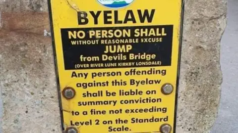 Cumbria Police A yellow sign reading: "BYELAW No person shall without reasonable excuse jump from Devils Bridge".