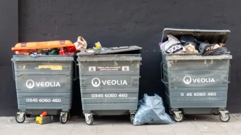 Three large grey industrial waste bins in a row with words Veolia written on each bin