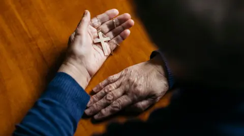 File photo of someone holding a cross in their palm while seated at a table