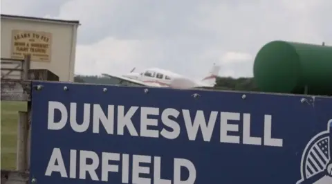 BBC The airport sign saying Dunkeswell Airfield on a gate
