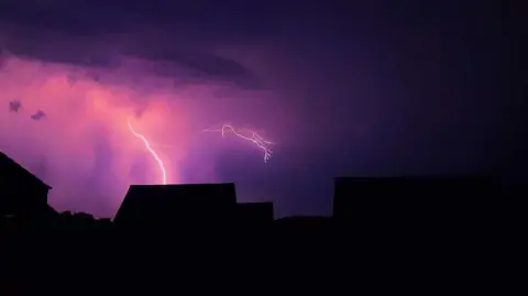 Mel Williams-Siddons Lightning in a pink sky over some homes.