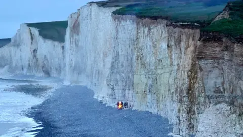 Sy Martin Birling Gap cliffs with four people gathered around a fire on the beach below.