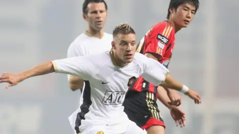 Getty Images Footballer Alan Smith playing for Manchester United, while team-mate Ryan Giggs and an opposing player, watch on from behind him.