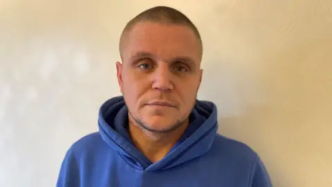 Emma Glasbey/BBC A bald man wearing a blue hooded sweatshirt.