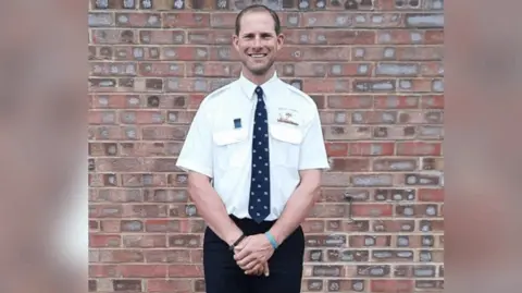 RNLI W.G Cooper's grandson standing hand in hand in his RNLI uniform-a shirt and tie. He is smiling.