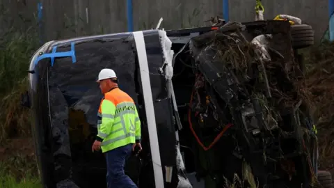 An emergency worker walks past the wreckage of a vehicle at the site of a bus accident 