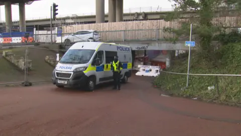 BBC van polisi dan petugas polisi dengan underpass di mana seorang wanita diserang dan diperkosa. Underpass disegel, saat mobil melaju di jalan di atasnya