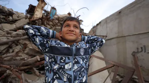 BBC Zakaria wears a blue and white hood for sitting in a little demolition and puts his hands on their hands while smiling.