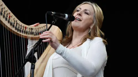 Getty Images Moya Brennan performing live, singing and playing a harp. She is in a white top.