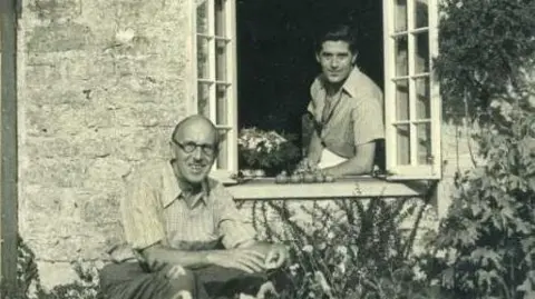 Dorset Museum and Art Gallery A black and white image of Norman Notley and David Brynley at the window of their stone cottage