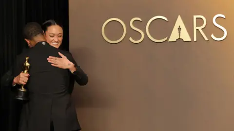 Getty Images Autumn Durald Arkapaw smiles as she hugs Michael B Jordan, while clutching the Academy Award for best cinematography, next to a sign reading 'Oscars' on the wall next to them, onstage during the ceremony awards.