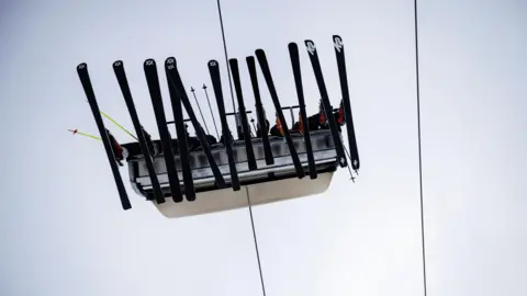 Reuters Six people in a chairlift. We can only see their skis from below. Two wires are above. 