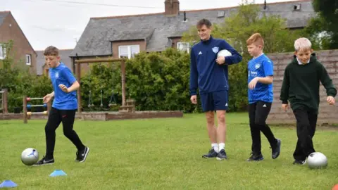 Partner School Programme Pupils and coach dribbling footballs.